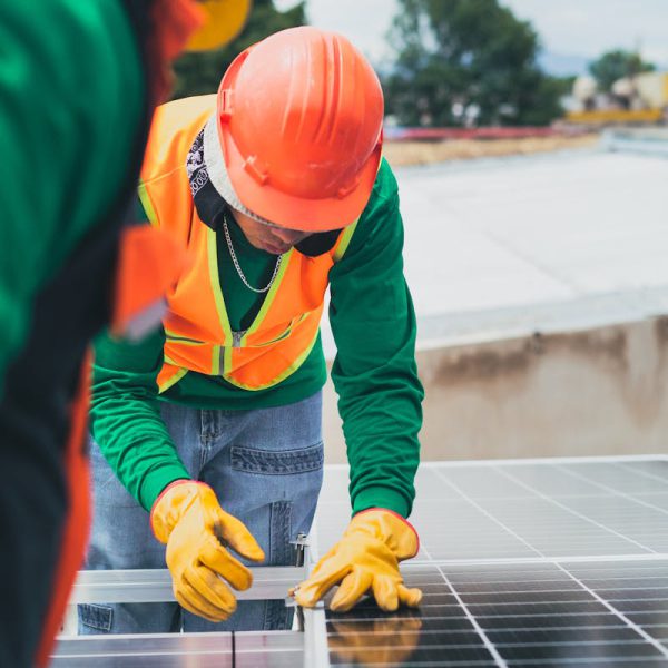 Worker in safety gear installing solar panels on a rooftop.